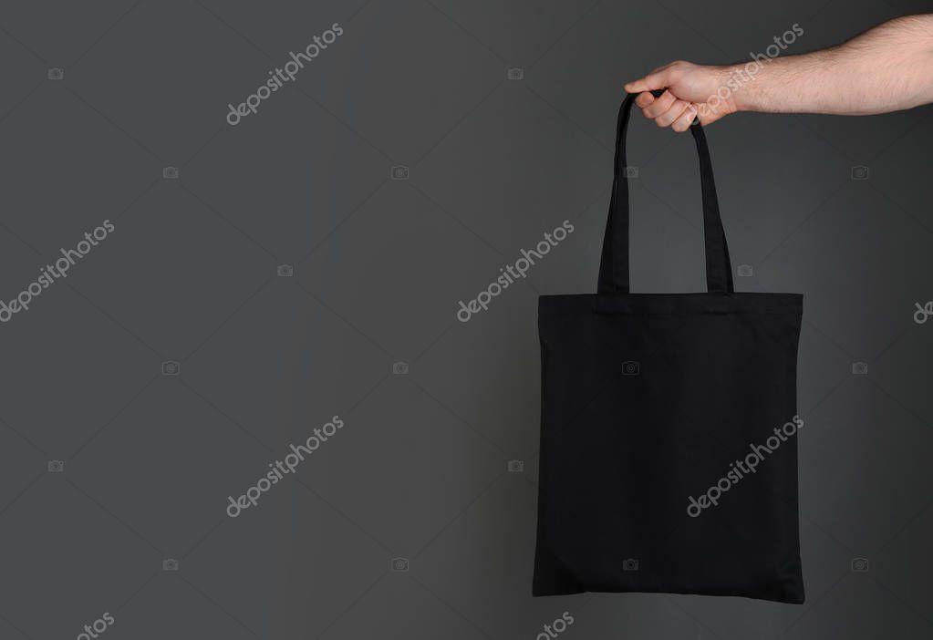 Man holding cotton shopping eco bag on grey background. Mockup for design