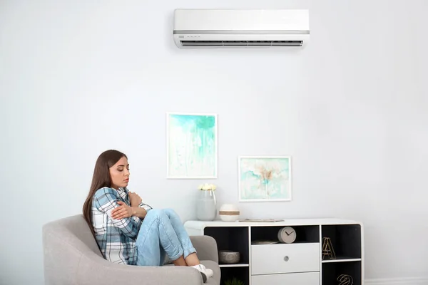 Young woman suffering from cold near broken air conditioner at home