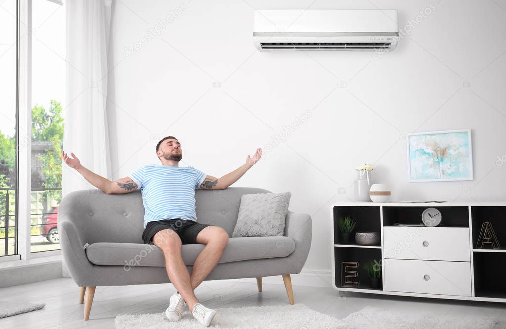 Young woman suffering from cold near broken air conditioner at home