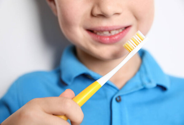 Little boy with toothbrush on light background, closeup