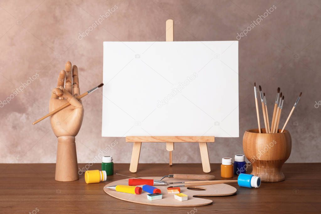 Wooden easel with blank canvas board and painting tools for children on table near color wall