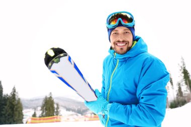 Happy couple with ski equipment sitting on snowy hill in mountains, space for text. Winter vacation