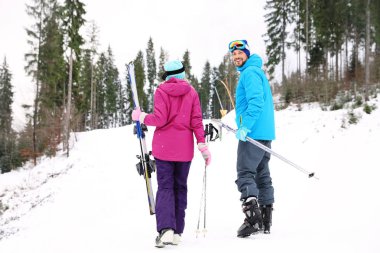 Happy couple with ski equipment sitting on snowy hill in mountains, space for text. Winter vacation