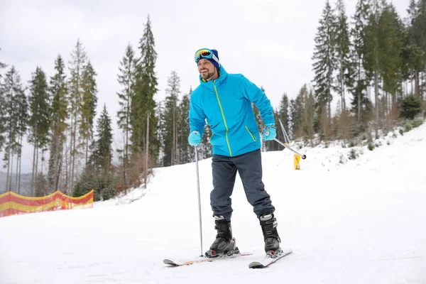 Happy couple with ski equipment sitting on snowy hill in mountains, space for text. Winter vacation