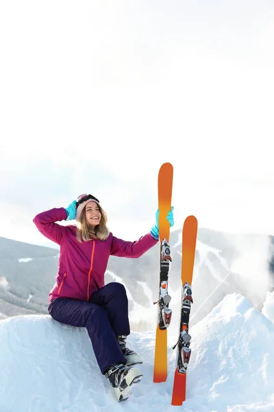 山の雪の吹きだまりに座ってスキー用具を持つ若い女性 冬の休暇 — ストック写真
