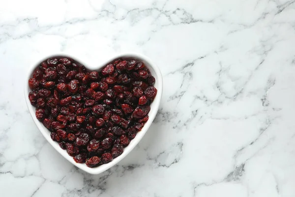 Heart shaped bowl with cranberries on marble table, top view with space for text. Dried fruit as healthy snack