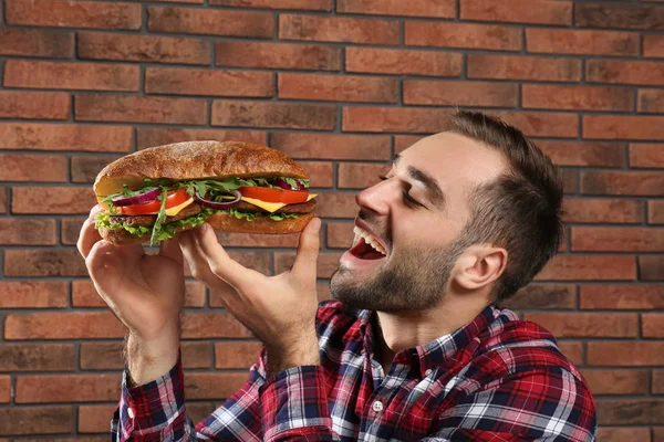 Jovem Faminto Homem Comer Saboroso Sanduíche Tijolo Parede Fundo — Fotografia de Stock