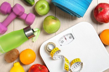 Flat lay composition with scales, healthy food and sport equipment on wooden background. Weight loss