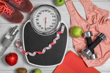 Flat lay composition with scales, healthy food and sport equipment on wooden background. Weight loss