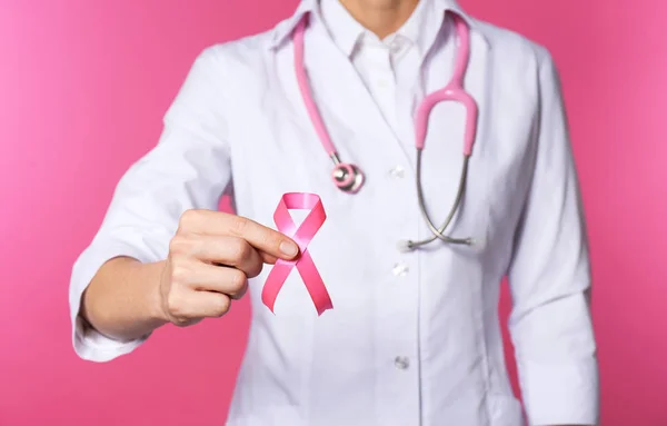 Female doctor with pink ribbon and stethoscope on white background, closeup. Breast cancer concept