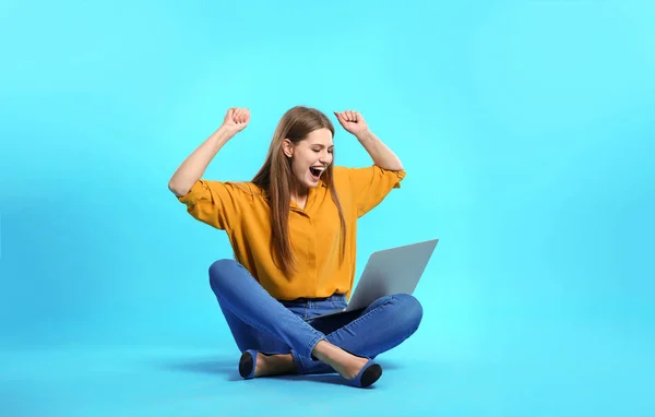 Emotional young woman with laptop celebrating victory on color background