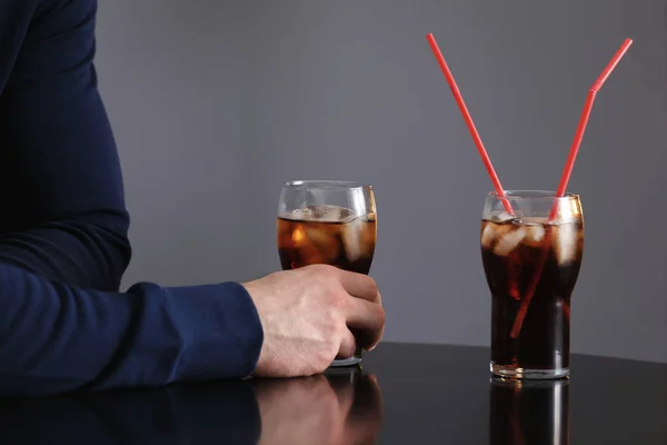 クローズ アップ 灰色の背景に対してテーブルでアイス コーラのグラスを持つ男 — ストック写真