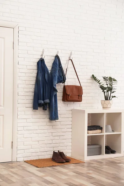 Stylish hallway interior with comfortable furniture and clothes on brick wall