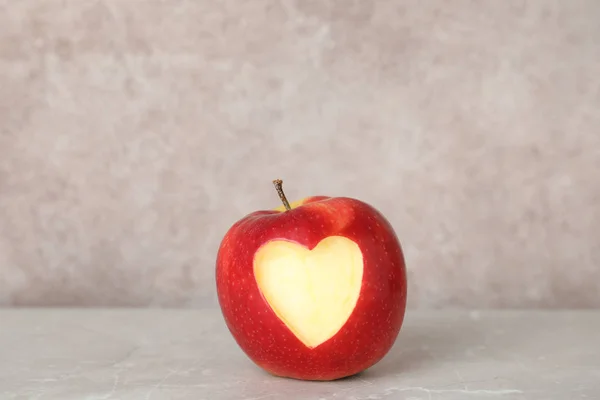 Red apple with carved heart on table against grey background