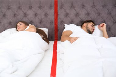 Ayrı ayrı evde yatakta yatan ilişki sorunları olan genç çift üzgün