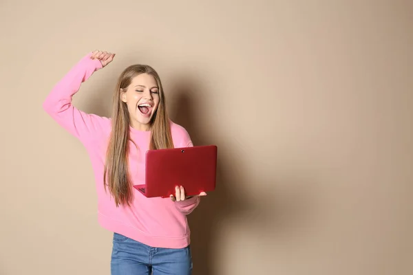 Emotional young woman with laptop celebrating victory on color background. Space for text