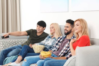 Gençler evde kanepede televizyon izlerken atıştırmalıklar ile