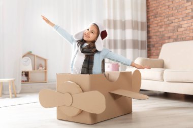 Oturma odasında karton uçak ile oynayan sevimli küçük kız