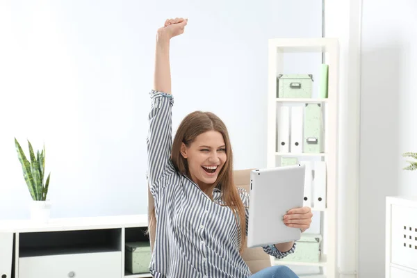 Emotional young woman with tablet celebrating victory in office