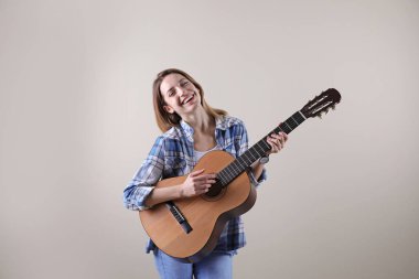 Genç kadın gri arka plan üzerinde akustik gitar çalmak