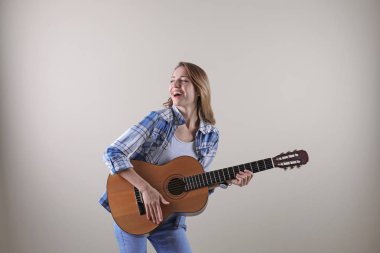 Genç kadın gri arka plan üzerinde akustik gitar çalmak