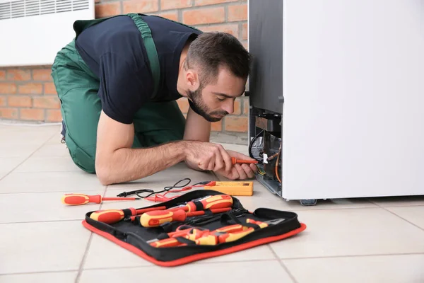 Male technician in uniform repairing refrigerator indoors