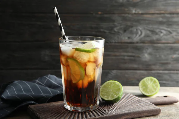 Glass of cocktail with cola, ice and cut lime on table