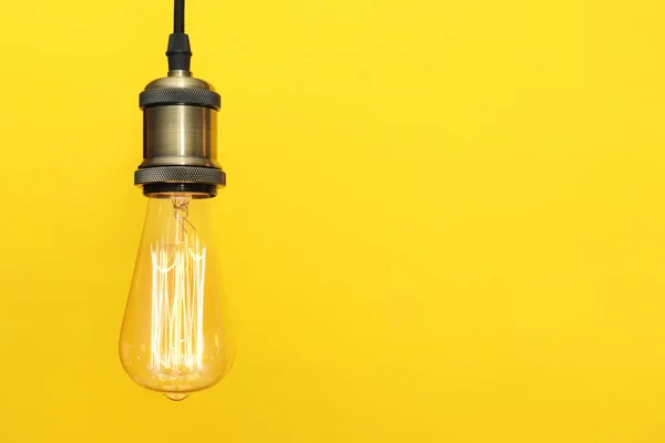 Pendant lamp with light bulb on color background, space for text