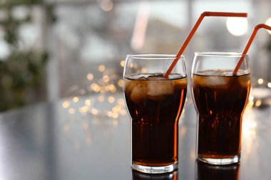 Glasses of cold cola against blurred fairy lights. Space for text clipart