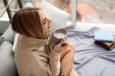 Örme kazak fincan kahve evde oturan güzel genç kadın. Kış atmosfer