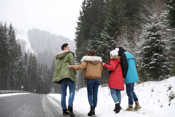 Group of excited friends with backpacks enjoying mountain view during winter vacation