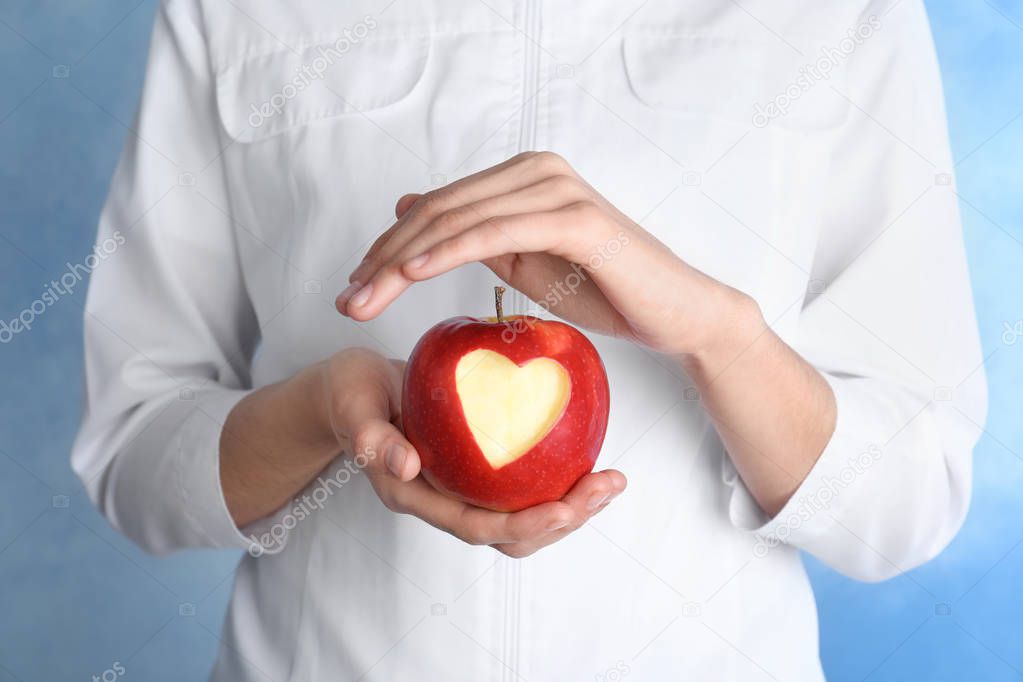 Woman holding apple with carved heart on color background, closeup