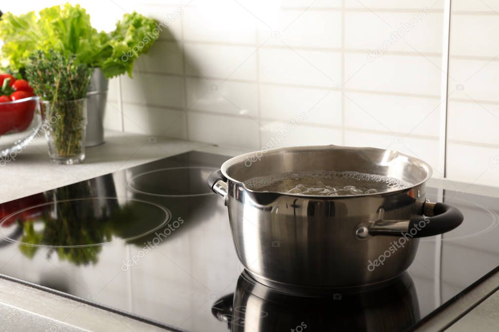 Pot with boiling water on electric stove in kitchen, space for text