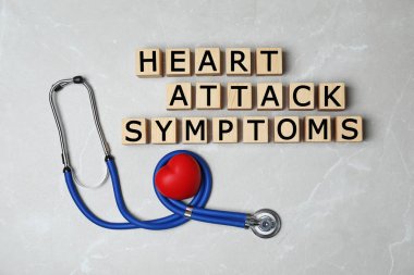 Düz ahşap küpleri ile metin kalp krizi belirtileri ve stetoskop gri arka plan üzerinde yatıyordu