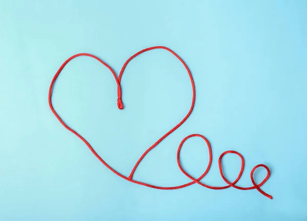Heart made of red string on light background, top view