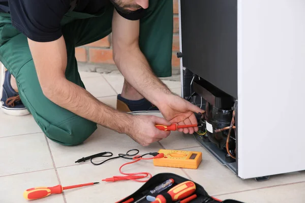 Male technician repairing broken refrigerator indoors, closeup