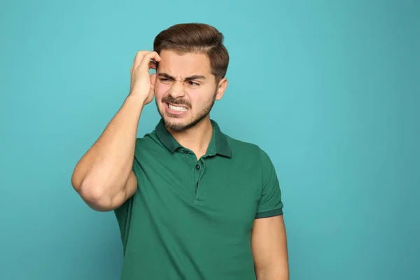 Young man scratching head on color background. Annoying itch