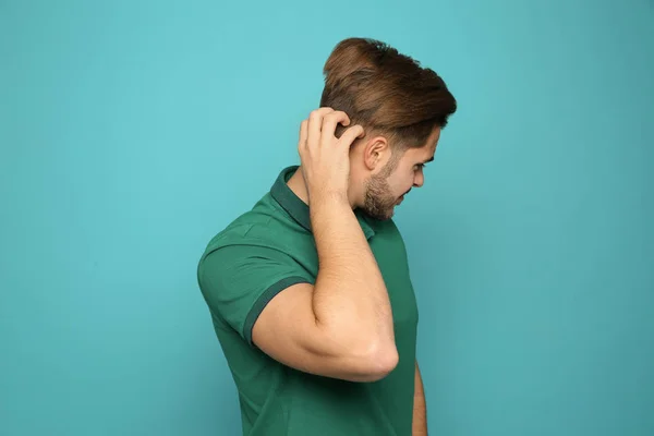 Young man scratching head on color background. Annoying itch