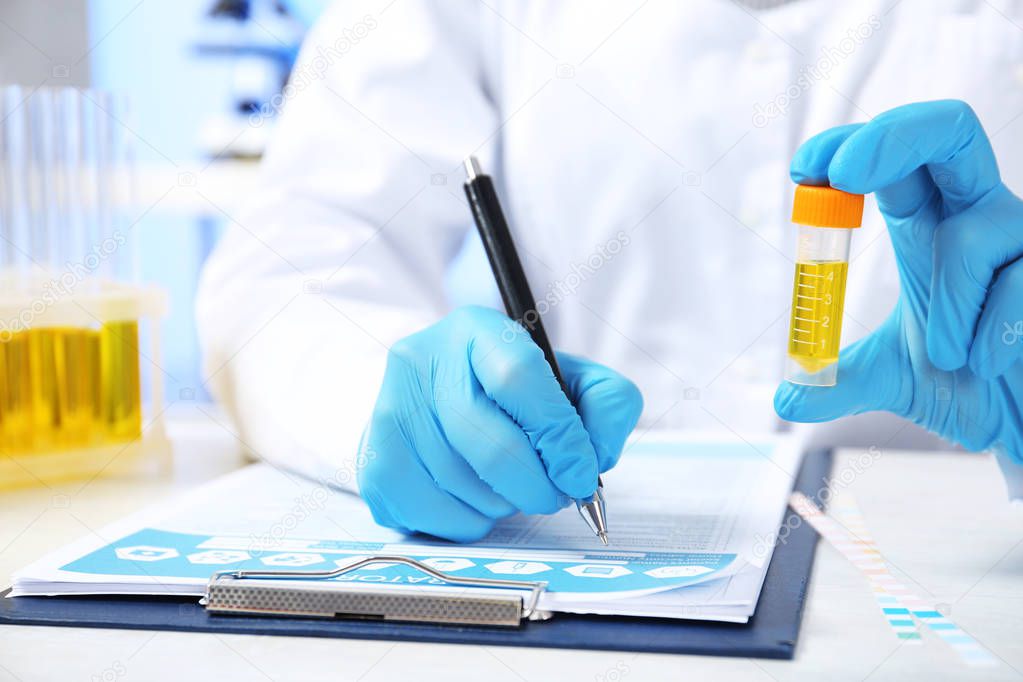 Laboratory assistant with urine sample for analysis writing results of tests at table indoors, closeup