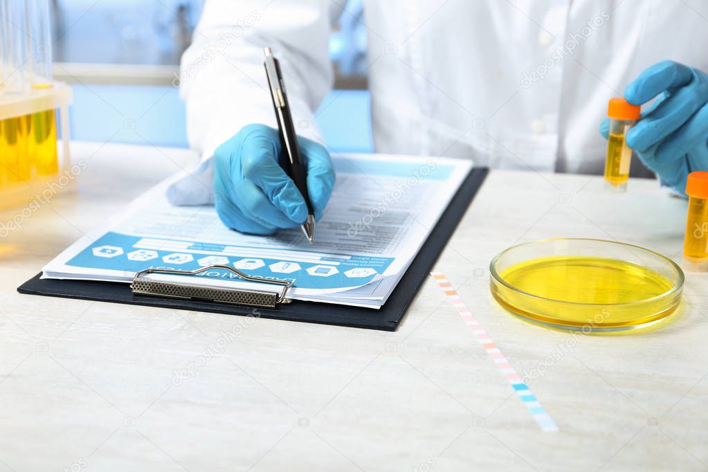 Laboratory assistant with urine sample for analysis writing results of tests at table indoors, closeup