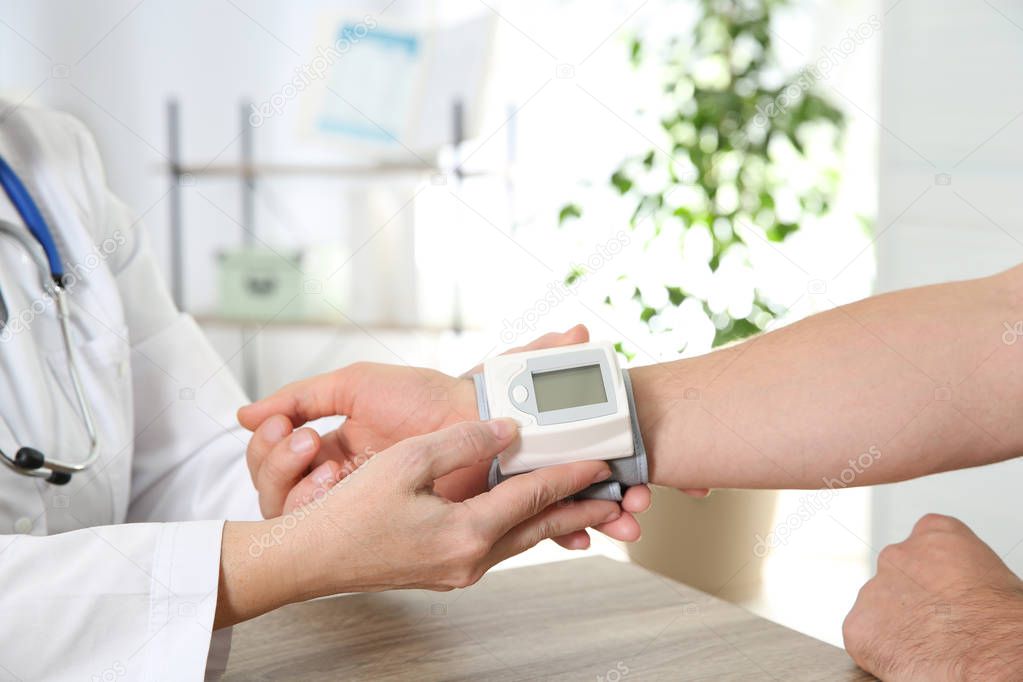 Doctor checking man's pulse with medical device in hospital, closeup