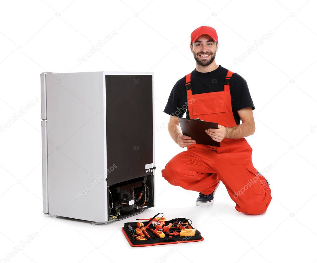 Male technician with clipboard and tools near broken refrigerator on white background