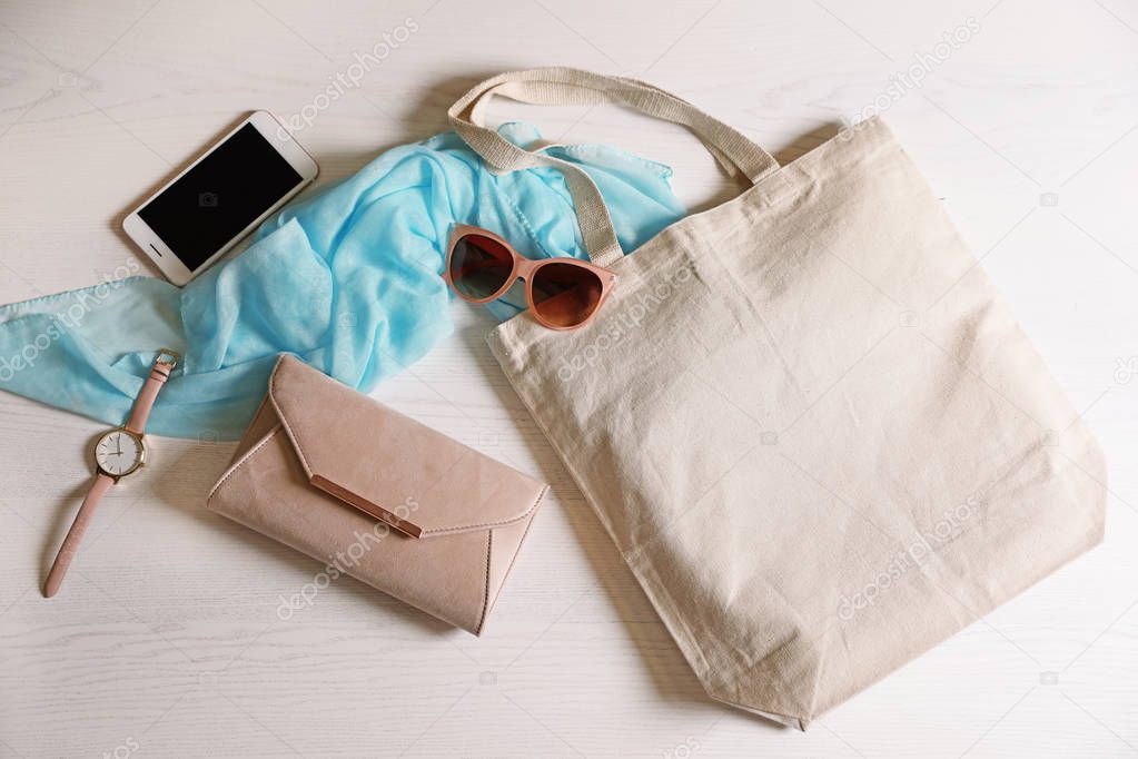 Flat lay composition with eco tote bag, smartphone and accessories on white wooden background. Space for design