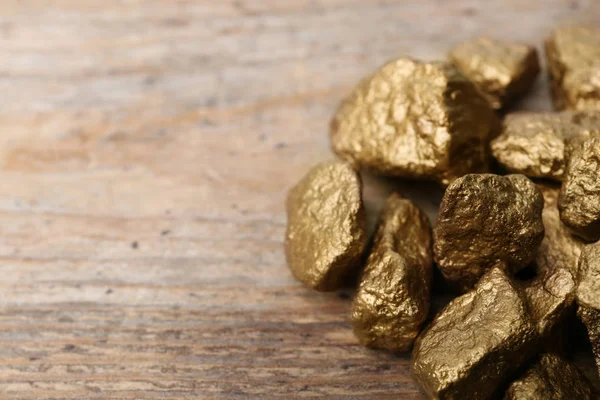 Pile of gold nuggets on wooden background. Space for text