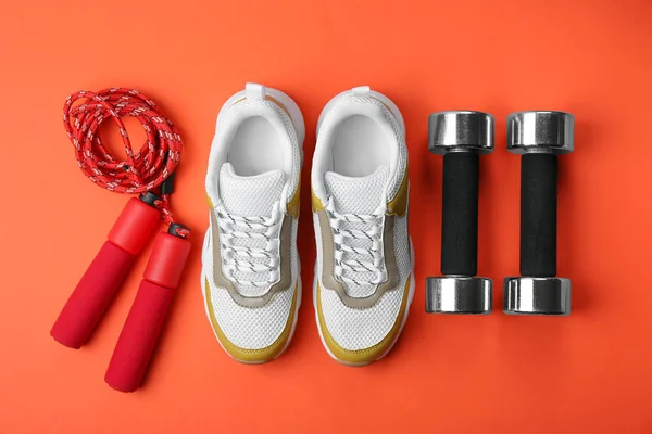 Flat lay composition of training shoes, dumbbells and jump rope on color background