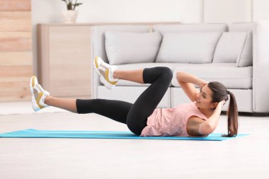 Evde egzersiz yaparak fitness giysili genç kadın