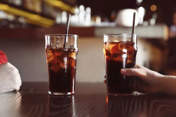 Young couple with glasses of refreshing cola at table indoors, closeup