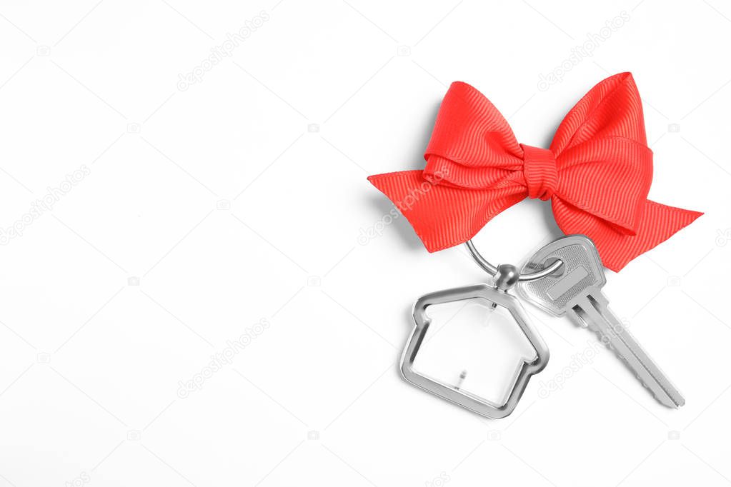 House key with trinket and bow on white background, top view. Space for text
