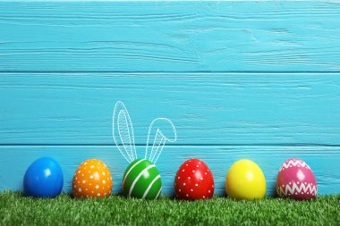 Paskalya yumurtaları ve sevimli tavşan'ın kulakları ahşap arka plan karşı yeşil çimlerin üzerine dekore edilmiştir. Metin için yer 