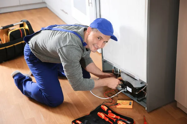 Male technician in uniform repairing refrigerator indoors